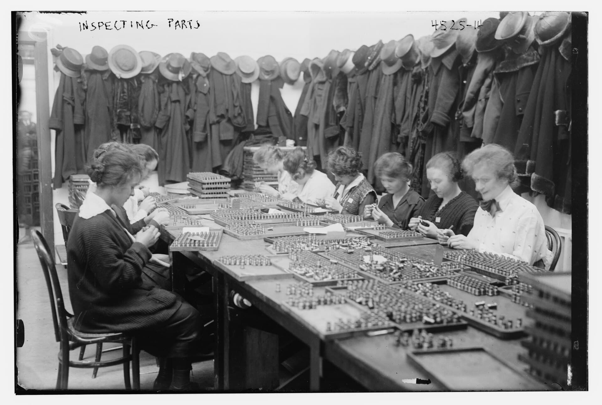 Women inspecting machine parts laid out in rows on long tables, 1915